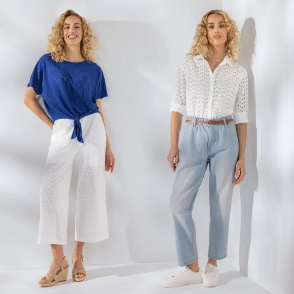 Zwei Frauen modellieren stilvolle Outfits: die eine in einem blauen Oberteil und einer weißen Culottes, die andere in einer weißen Bluse und einer hellblauen Hose vor einem hellen Hintergrund.