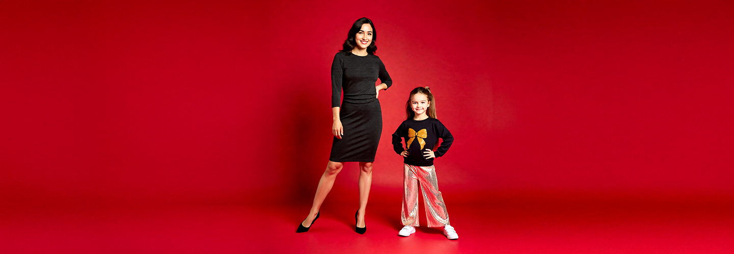 Eine Frau und ein Kind posieren vor einem leuchtend roten Hintergrund und tragen passende Lilo & Stitch T-Shirts und lässige Jeans